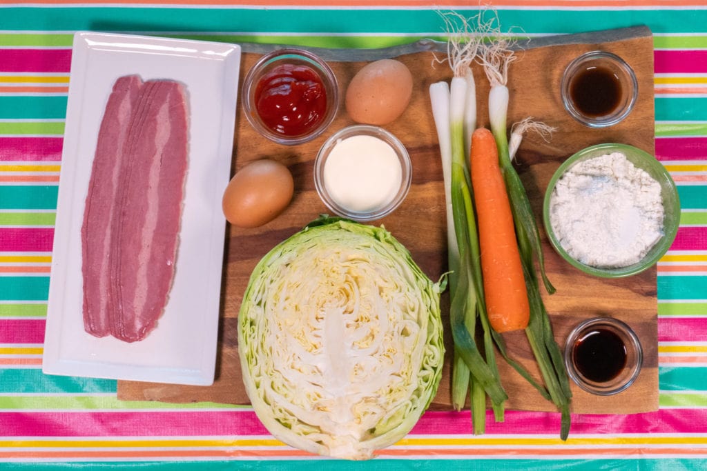 Ingredientes del okonomiyaki expuestos, adaptados para los niños: bacon de pavo, col rallada, zanahoria, cebollas verdes e ingredientes de la salsa okonomiyaki casera.