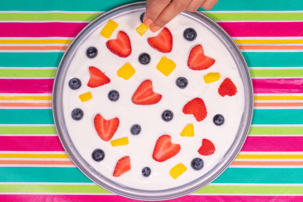 Montaje de la pizza fría de yogur con frutas, añadiendo los ingredientes 