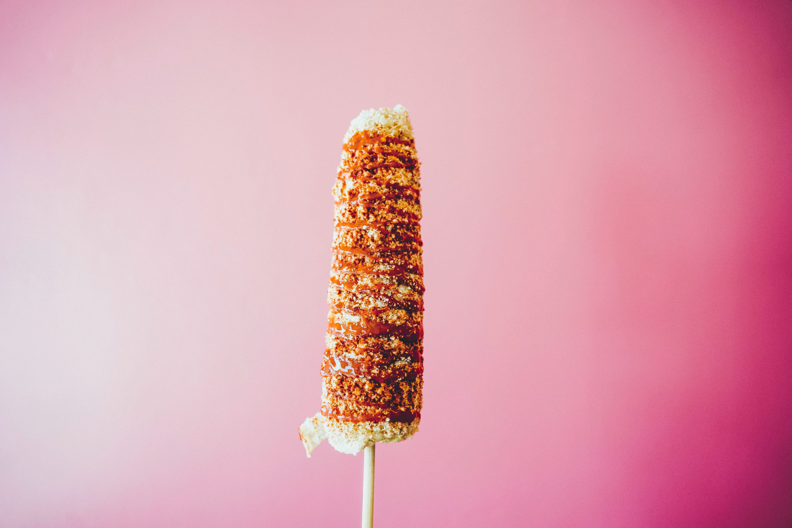 A elote over a pink background. Picture by Diego Lozano on Unsplash