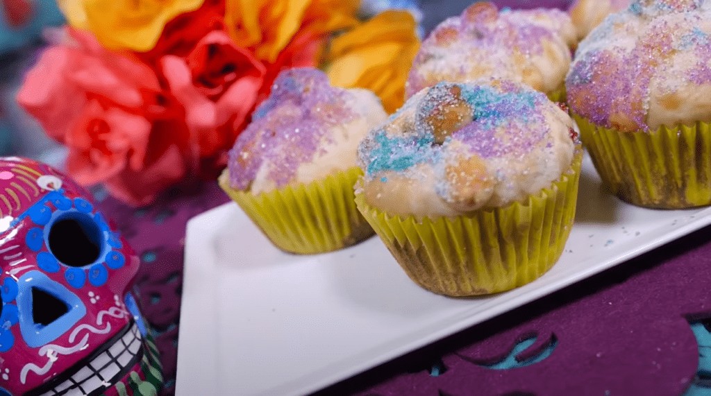 Pan de Muerto cupcakes served on a white platter, next to a decorated skull for Día de Muertos
