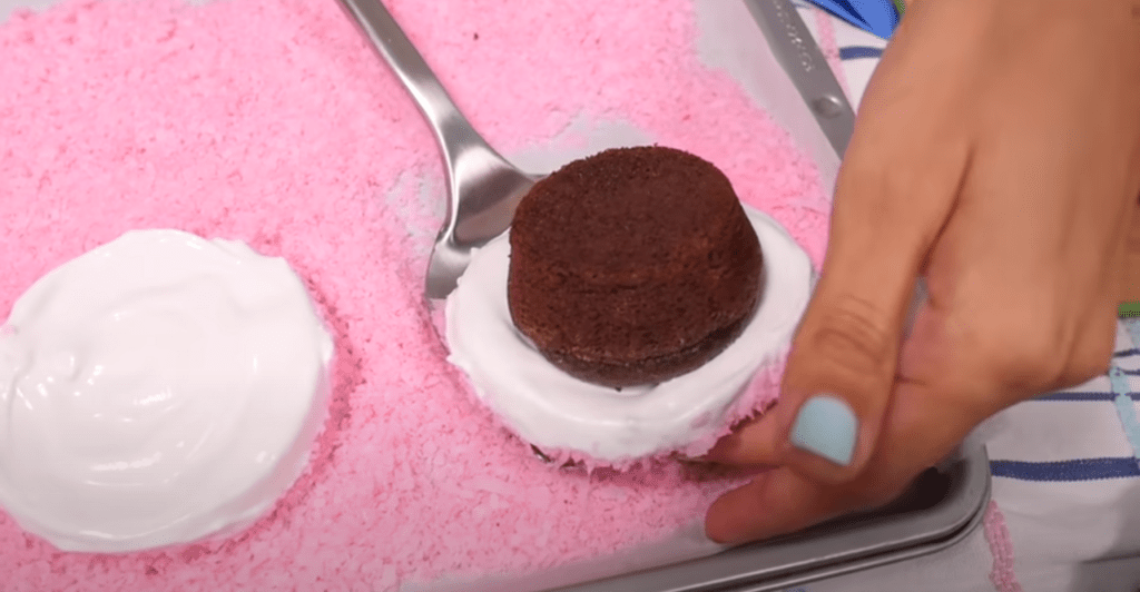 Covering a chocolate cupcake with marshmallow and pink coconut shavings to make a Fat Cake